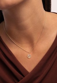 Collana in oro con ciondolo rotondo impreziosito da pietre scintillanti multicolori. Il ciondolo ha una superficie liscia e un piccolo gancio.