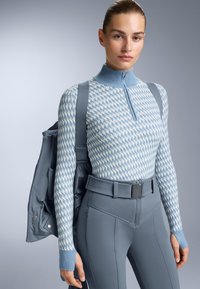 Ljusblå stickad tröja med hög krage, med ett geometriskt mönster. Kombinerad med ljusgrå tajta byxor och en grå axelväska.