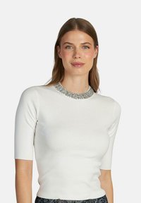 Top bianco a maniche corte con un design aderente e dettagli in collare argentato decorato. Texture liscia e silhouette pulita.