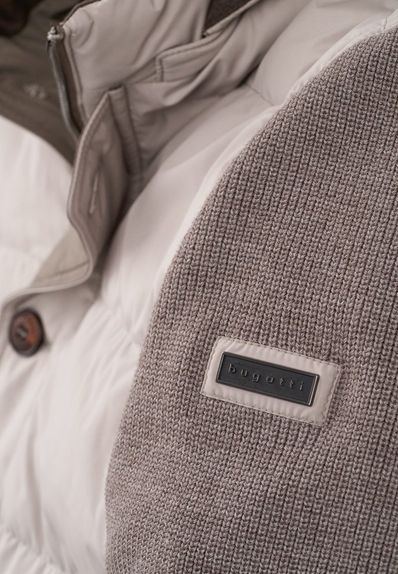 Padded jacket z dzianinowym szarym rękawem, kremowym przodem, brązowymi guzikami oraz czarną metką marki.