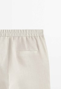 Ljusbeiga, byxor med elastisk midja gjorda av texturerat tyg, med en enda bakficka och enkel design utan synliga knäppningar.