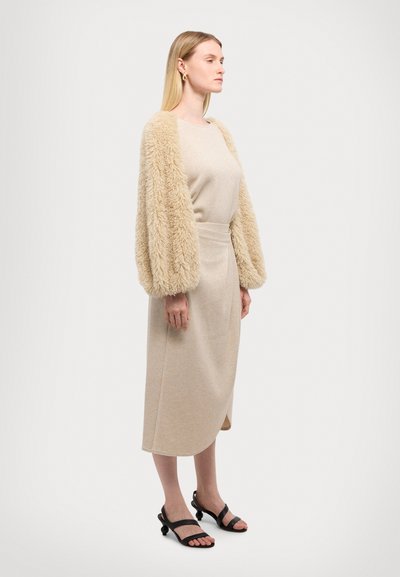 Knee-length beige dress with a fitted silhouette and plush, fluffy beige sleeves. Worn with black strappy sandals. Smooth texture and simple design.