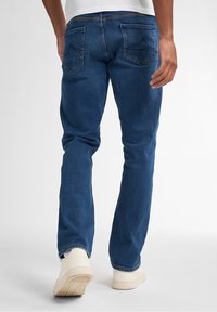 Jeans in denim blu scuro con taglio dritto, dotati di due tasche posteriori, leggeri segni di usura e abbinati a sneakers bianche.