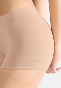 Boyshorts in tessuto elasticizzato beige con una superficie liscia e un discreto dettaglio del logo. La fascia in vita si trova appena sopra i fianchi.