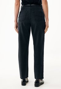 Jeans de denim negro con corte recto, cinco bolsillos y cintura alta. La tela parece resistente, con un mínmo desgaste y bordes limpios.
