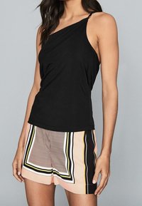 Top sans manches noir avec une seule bretelle, associé à un short rose clair comportant des motifs géométriques et de larges rayures accentuées en noir et jaune.