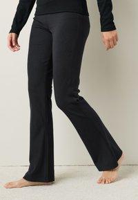 Pantalones acampanados negros confeccionados con tela elástica, que presentan una textura lisa, detalles visibles de costuras y una cintura entallada.