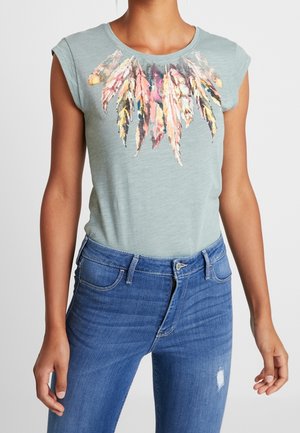 Helles grünes T-Shirt mit rundem Ausschnitt und kurzen Ärmeln, das ein farbenfrohes Federdesign zeigt. Kombiniert mit blauen Jeans.