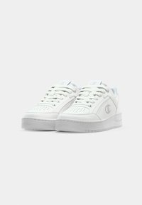 White leather sneakers with perforated toe, round laces, and padded collar. Features a raised white sole and silver logo on the side.