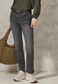 Jeans in denim grigio con una vestibilità slim, caratterizzati da tasche frontali e un delicato dettaglio di cucitura, abbinati a sneaker beige e una borsa a spalla marrone.