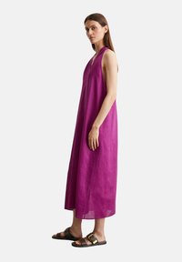 Robe longue sans manches avec encolure en V en lin violet vif. Dotée d'une coupe ample avec des poches latérales, accompagnée de sandales sombres.