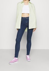 Světle zelená oversized košile, bílý croptop, tmavě modré skinny džíny a růžové tenisky s bílými podrážkami a pruhy.