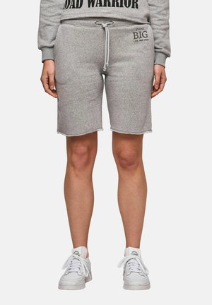 Person wearing light grey knee-length shorts with drawstring, matching sweatshirt, and white sneakers, standing against a plain background.