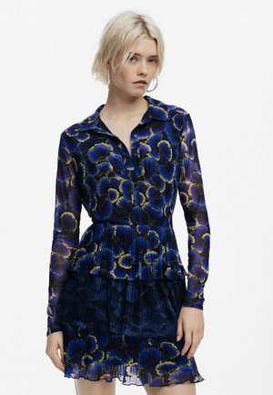 Floral patterned dress featuring a collared neckline, long sleeves, and a pleated skirt with ruffles. Colors include deep blue and gold accents.
