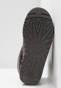 Semelle en caoutchouc noir d'une botte UGG affichant un motif à rayons de soleil et le logo UGG au centre.