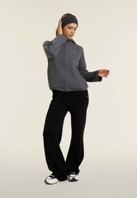 Veste zippée grise avec un motif en tricot torsadé texturé, accompagnée de pantalons larges noirs et de baskets noires, sur fond neutre.