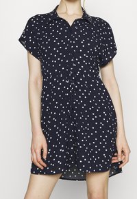 Abito navy a maniche corte con pois bianchi, chiusura a bottoni sul davanti, vita legata e silhouette ad A, realizzato in tessuto leggero.