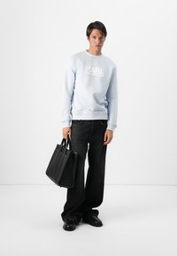 Sudadera azul claro con el logo "KARL LAGERFELD", combinada con jeans de pierna ancha negros y un gran bolso negro con múltiples compartimentos.