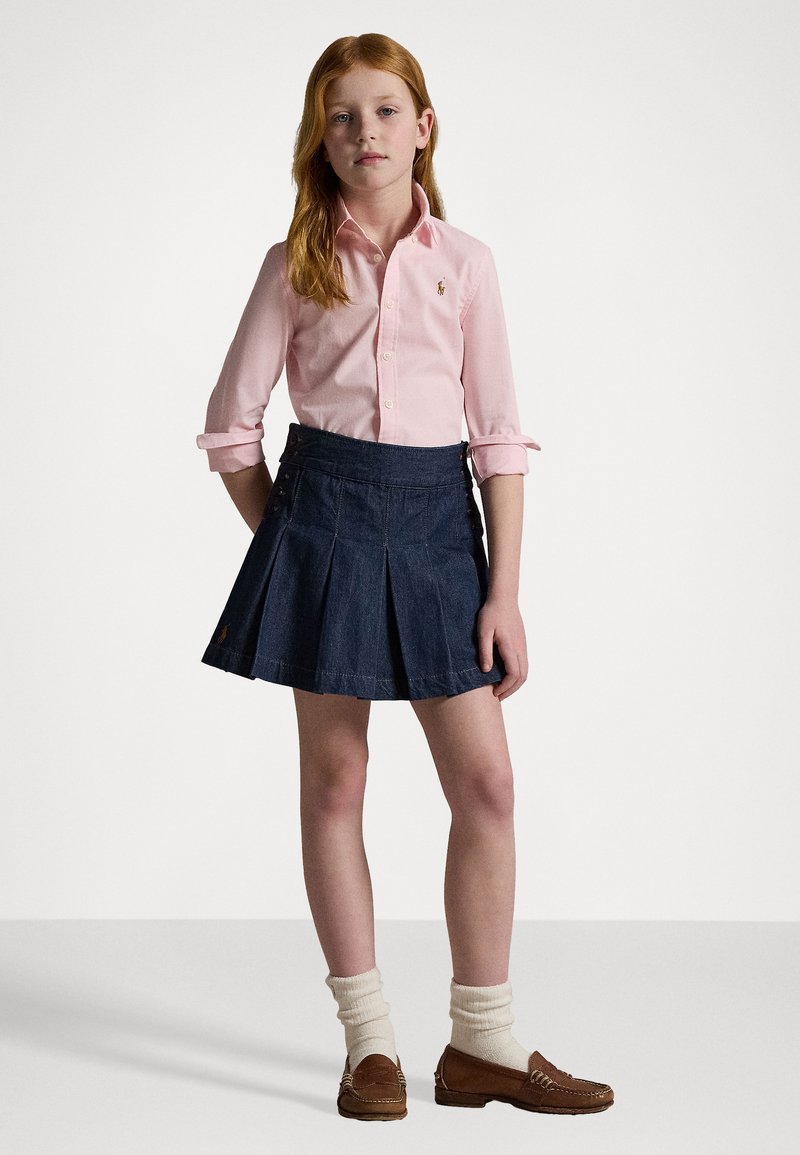Lys rosa langermet skjorte, marineblå plissert denimsirkel, brune loafers og hvite sokker. Sirkelen har knapper i midjen.