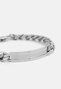 Bracciale in argento con una placca centrale piatta caratterizzata dall'incisione "HILFIGER". Il design a catena è texturizzato e lucidato.