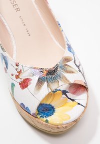 Gros plan d'une chaussure compensée à bout ouvert avec un motif floral, une finition brillante craquelée et une semelle en liège.