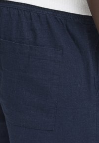 Tmavomodré ľanové nohavice s elastickým pásom a náprsným vreckom na boku. Tkanina má jemný textúrovaný vzor.
