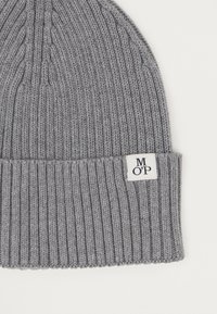 Hallatud hallist kudumist beanie, ribatud tekstuuriga ja volditava servaga, millel on väike valge silt, millel on tikitud tähed "M O' P".