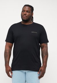 Sort bomulds T-shirt med korte ærmer, rund hals og lille guld tekst på brystet. Stof er glat med en afslappet pasform.