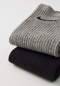 Deux paires de chaussettes côtelées : l'une en gris foncé avec un petit logo noir, et l'autre en noir uni, mettant en valeur un tissu texturé.