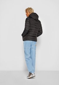Puffjakke i sort med horisontal quiltet design, hætte, parret med lyseblå løstsiddende jeans og multikolore sneakers.