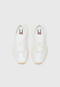 White sneakers with reflective accents, mesh fabric, and leather overlays. Light tan sole, featuring a patterned inner lining in navy, white, and red.
