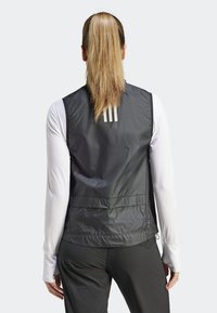 Czarna bezrękawnik o gładkiej fakturze, z trzema białymi paskami na plecach, noszona na białej koszuli z długim rękawem.