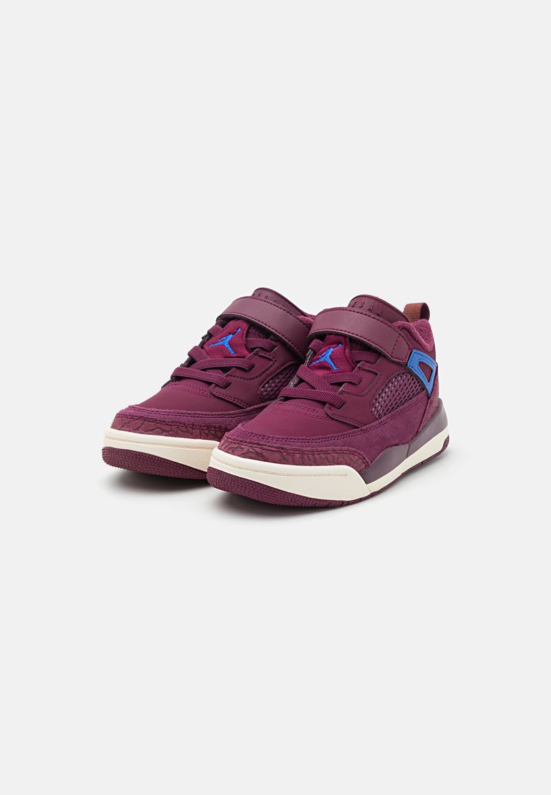 Zapatillas deportivas moradas con material de malla y sintético, correa ajustable, suela de goma, acentos estampados y logo azul en contraste.