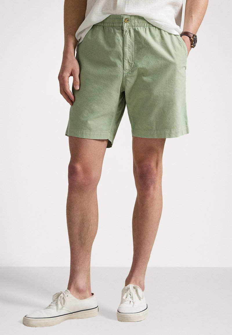 Shorts verts clairs en coton avec une taille élastique et un bouton à l'avant. Texture lisse, longueur genou et coupe décontractée.