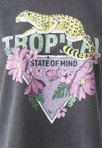 Šedá tkanina má grafický design se žlutým leopardem, květinami a textem "TROPICKÝ STAV MYSLI" v různých barvách a texturách.