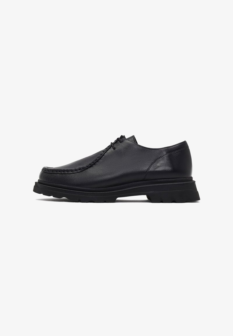 Chaussure à lacets pour homme en cuir noir avec semelle épaisse crantée et bout arrondi cousu, vue de profil sur fond blanc.