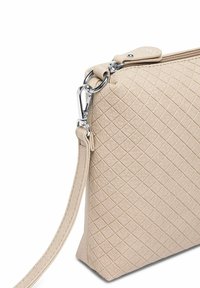 Béžová prošívaná kabelka s texturovaným povrchem, stříbrným kováním a odnímatelným popruhem, vybavená horním zapínáním na zip.