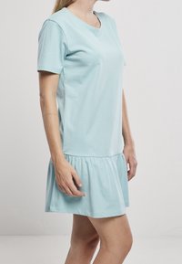 Vaaleansininen puuvillamekko, jossa on lyhyet hihat, rento istuvuus ja röyhelöhelma. Sujuva pinta ja pyöreäkaula-aukko. Näytetään sivuprofiilista.