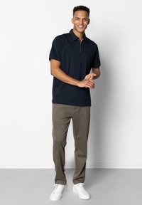 Polo navy à manches courtes avec un col zippé, associ�é à un pantalon léger beige et des baskets blanches, présenté sur un fond uni.
