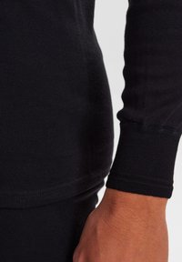 Black long-sleeve shirt featuring a ribbed texture, fitted cuffs, and a smooth body. The fabric appears soft and slightly stretchy.