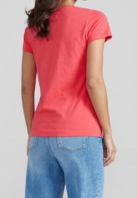 T-shirt corallo a maniche corte realizzato in cotone morbido, con scollatura rotonda e taglio dritto, abbinato a jeans blu chiaro a gamba dritta.