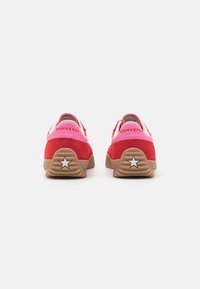 Baskets en suède rouges et roses avec une semelle texturée, présentant une étoile blanche sur le talon et le logo "CONVERSE" à l'arrière.
