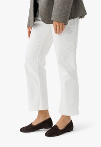 Mustadust mustad tossud ümarate varvastega ja minimalistliku disainiga, koos valgete sirgete pükstega ja tekstuuriga halli ülikondjacketiga.