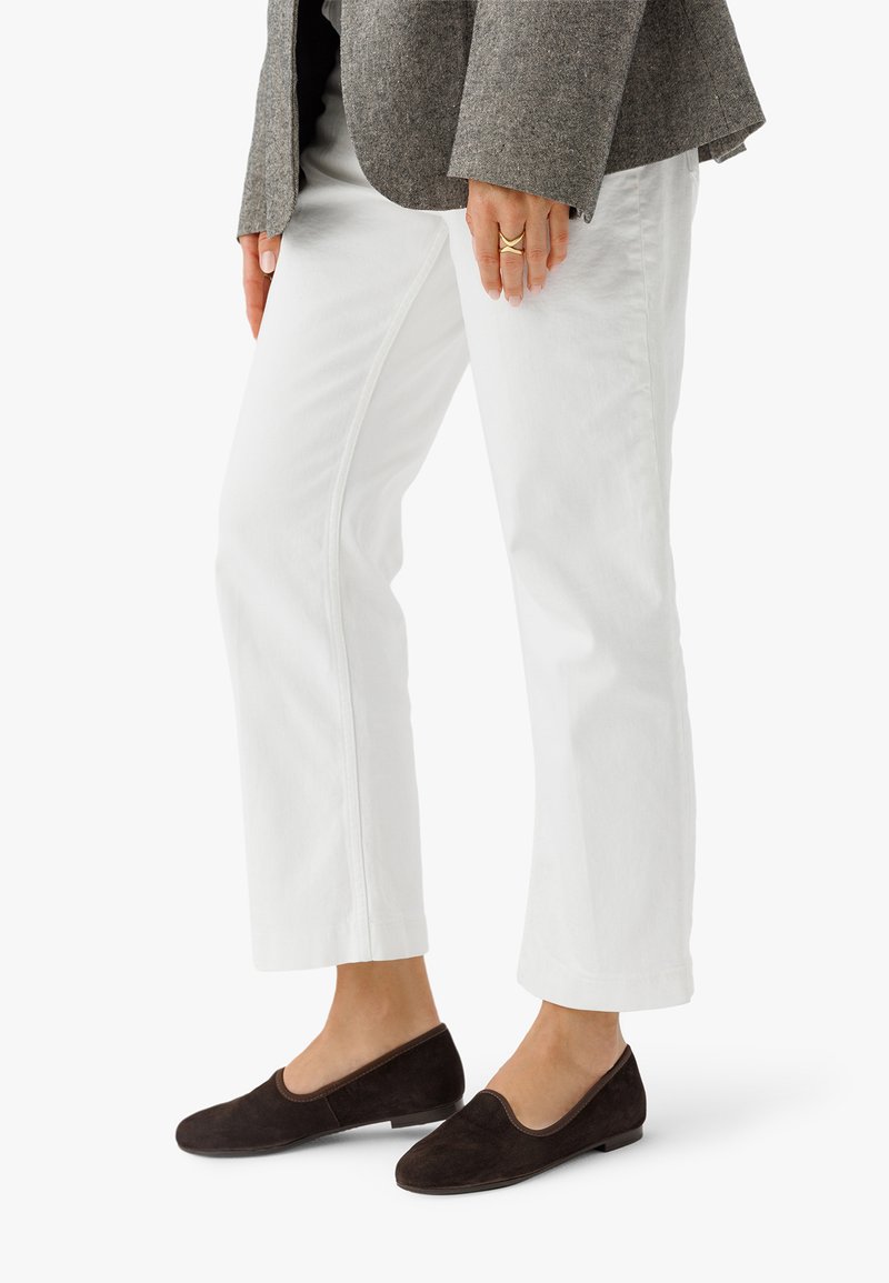 Mustadust mustad tossud ümarate varvastega ja minimalistliku disainiga, koos valgete sirgete pükstega ja tekstuuriga halli ülikondjacketiga.