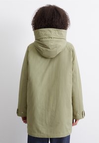 Ljusgrön vattentät parkas med huva, som har långa ärmar, en avslappnad passform och knäppte ärmslut. Slät textur och minimalistisk design.