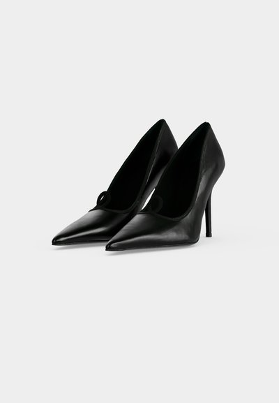 Paire de chaussures à talons hauts en cuir noir avec des bouts pointus et des talons aiguilles fins sur un fond clair uni.