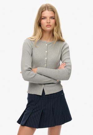 Grijze geribbelde cardigan met lange mouwen en ronde hals, met een knoopsluiting aan de voorkant. Gemaakt met een marineblauwe gestreepte rok.