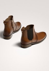 Brązowe skórzane botki za kostkę z elastycznymi bokami i tylnym zamkiem, cechujące się gładką teksturą i niskim obcasem dla stabilności.