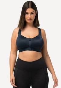 Sujetador deportivo navy con tirantes anchos y cierre frontal, fabricado en una tela suave. Combinado con leggings negros de cintura alta con costuras y bolsillos.