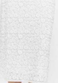 Jupe en dentelle florale blanche avec des appliqués de fleurs en couches, dotée d'une texture douce et d'une coupe ajustée, se terminant juste en dessous du genou.